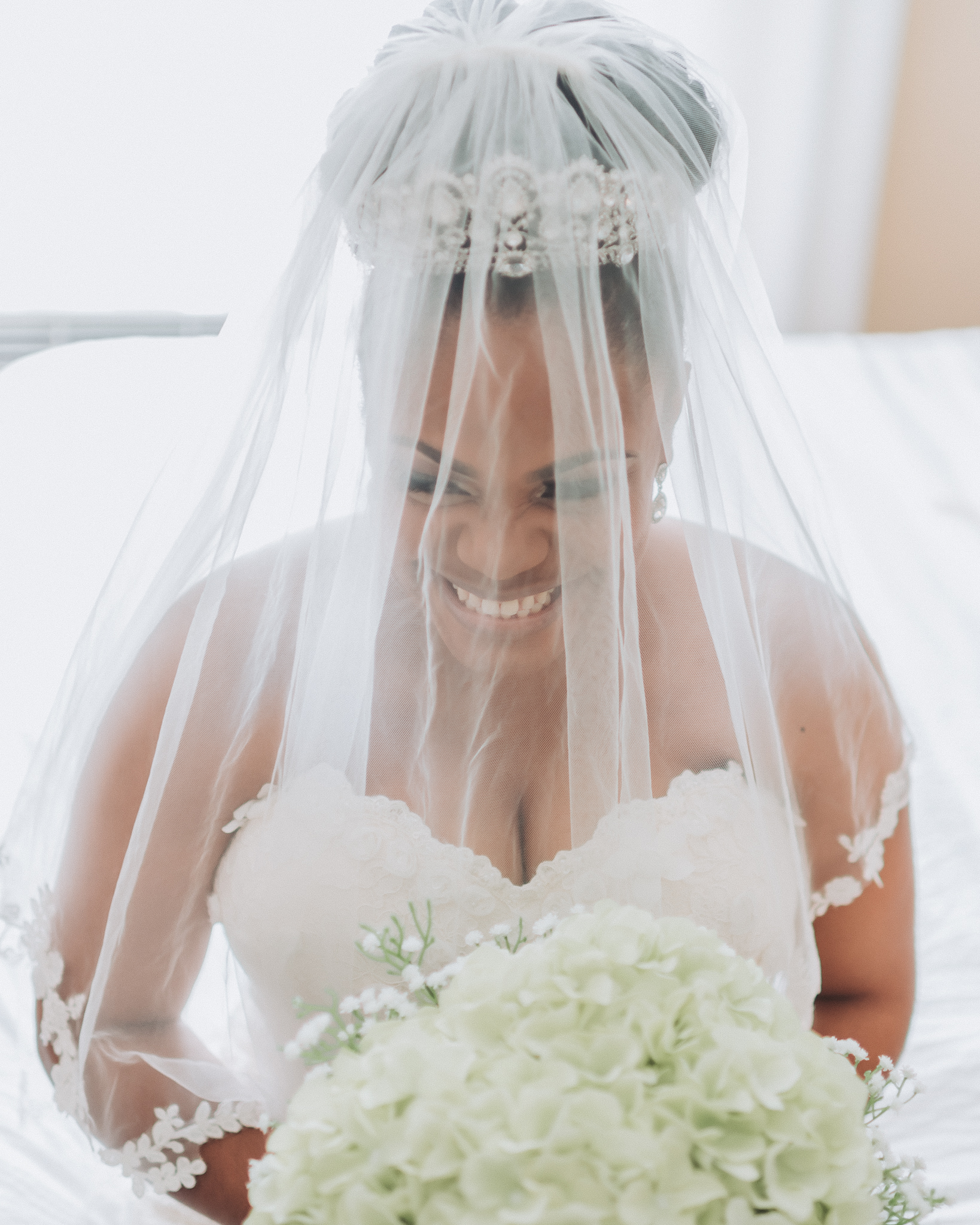Stunning bride with veil over her head, smiling from ear to ear. Waiting patiently to walk down the aisle