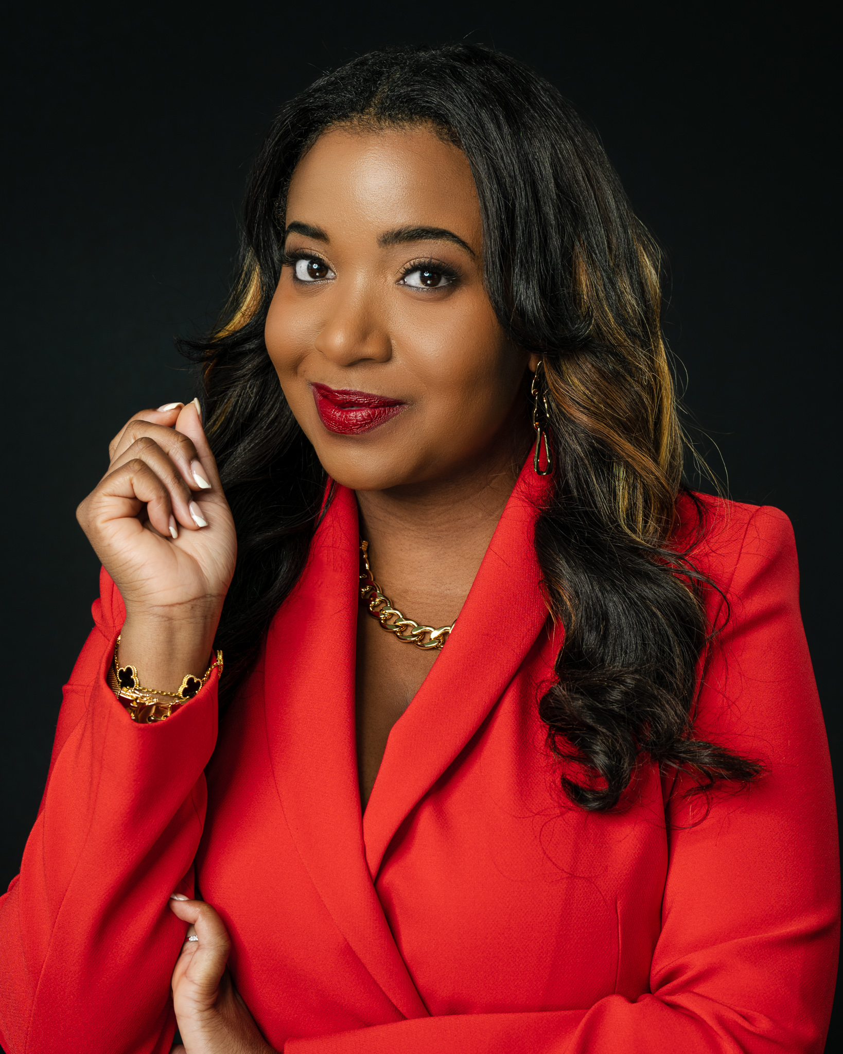 Professional Headshot taken of Client, dressed in a sophisticated red blazer, and against a black background.