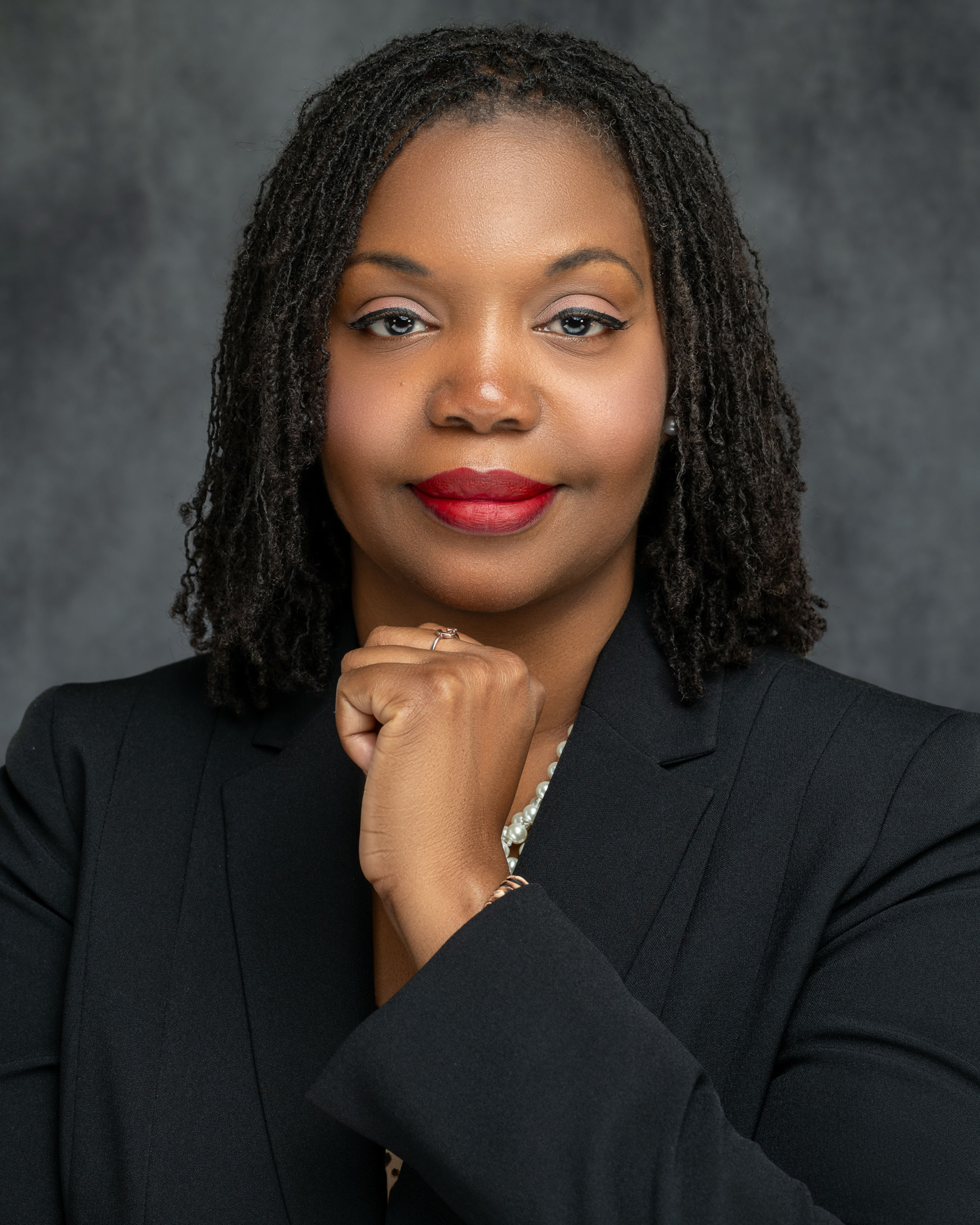 Attorney Headshots of Safiya Byars of The Byars Firms. She's wearing a black blazer with her arms folded and a grey background.
